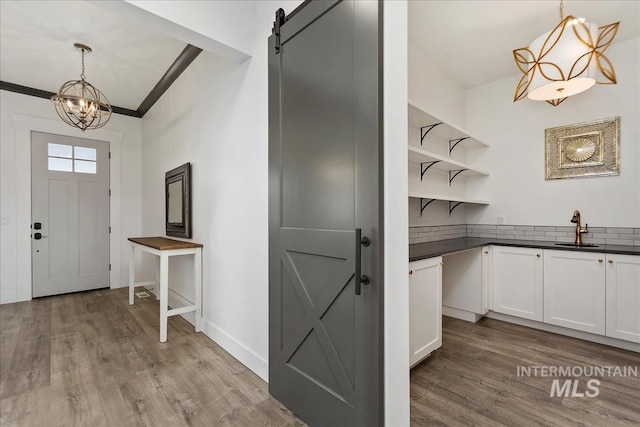 interior space with a barn door, a notable chandelier, baseboards, light wood-style floors, and crown molding