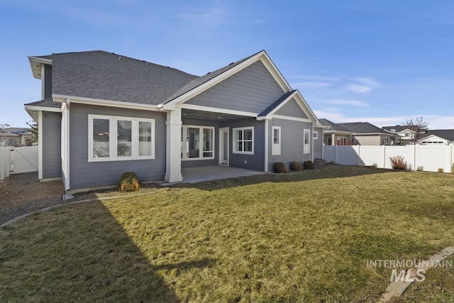 rear view of house featuring a patio area, a fenced backyard, a shingled roof, and a yard