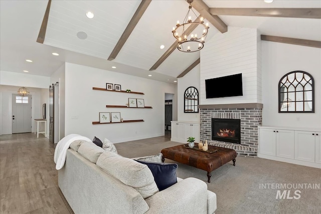 living area with a barn door, a glass covered fireplace, beamed ceiling, a notable chandelier, and recessed lighting