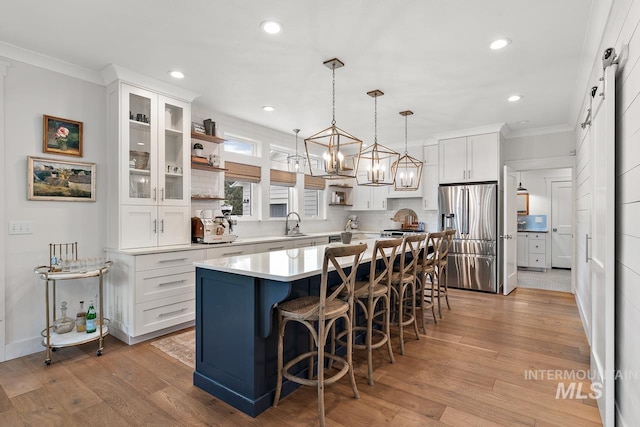 kitchen with stainless steel fridge, a breakfast bar, a barn door, a center island, and white cabinetry