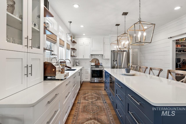 kitchen with stainless steel appliances, blue cabinetry, decorative light fixtures, white cabinets, and a center island