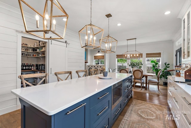 kitchen with wood walls, blue cabinets, a barn door, decorative light fixtures, and white cabinetry