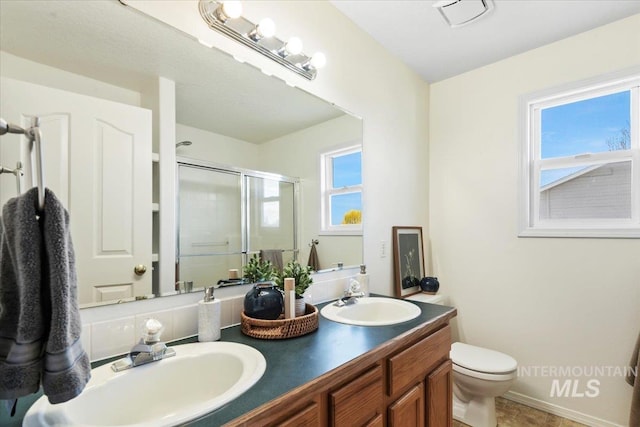 bathroom featuring toilet, a sink, a stall shower, and double vanity