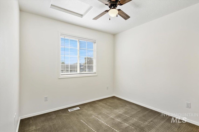 unfurnished room with a ceiling fan, attic access, dark colored carpet, baseboards, and visible vents