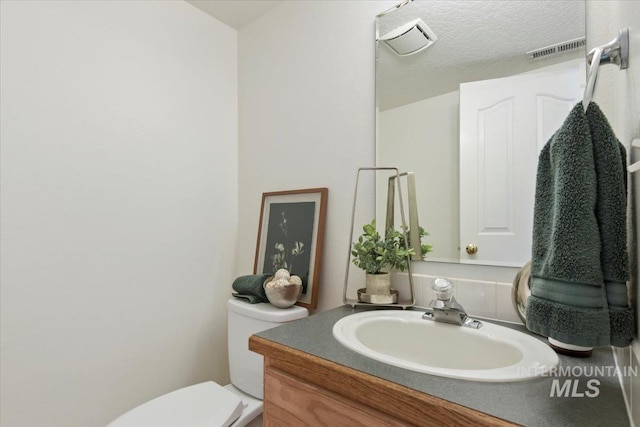 half bath with a textured ceiling, visible vents, toilet, and vanity