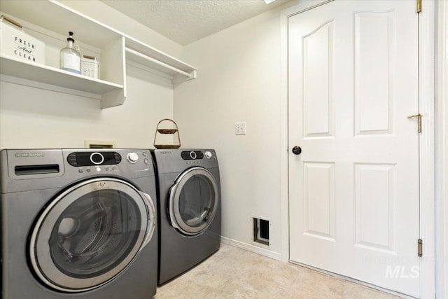 clothes washing area with baseboards, a textured ceiling, washing machine and clothes dryer, visible vents, and laundry area