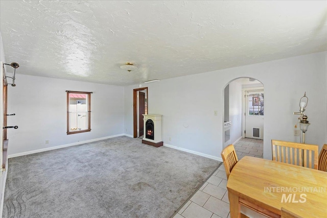 404 W 5th St, Weiser, ID 83672 - living room featuring arched walkways, baseboards, a textured ceiling, a warm lit fireplace, and light tile patterned floors