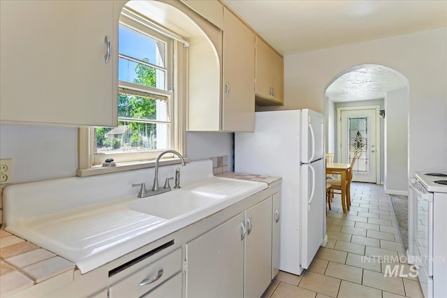 404 W 5th St, Weiser, ID 83672 - kitchen featuring arched walkways, a sink, white appliances, light tile patterned flooring, and light countertops
