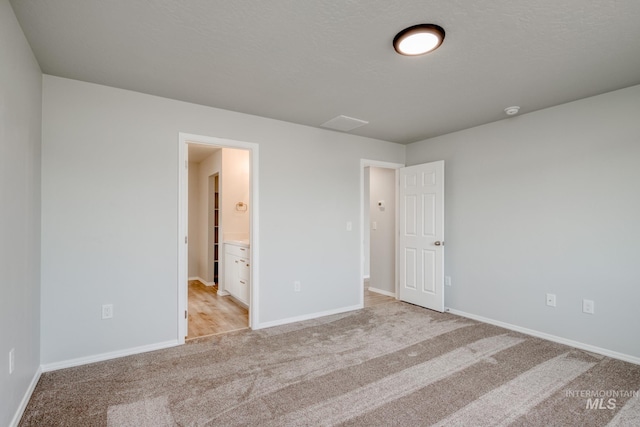 unfurnished bedroom featuring light carpet, a textured ceiling, ensuite bath, and baseboards