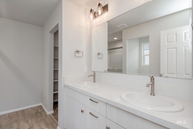 full bathroom with double vanity, a walk in closet, a sink, and wood finished floors