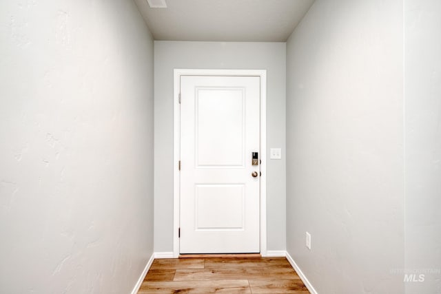 doorway with light wood-style floors, visible vents, and baseboards