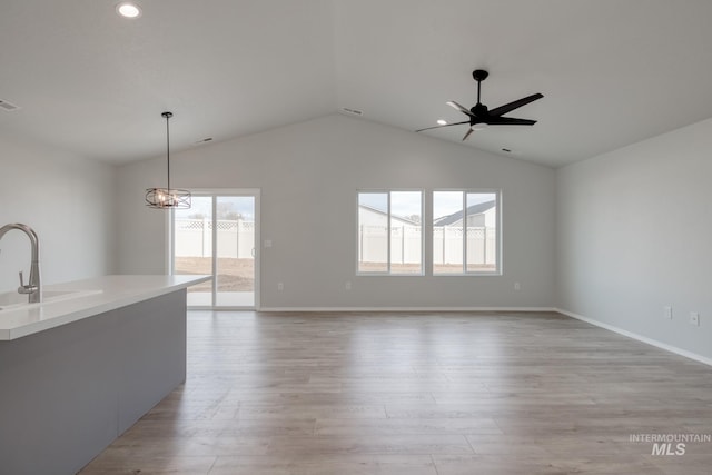 unfurnished living room with lofted ceiling, light wood-style flooring, ceiling fan with notable chandelier, a sink, and baseboards