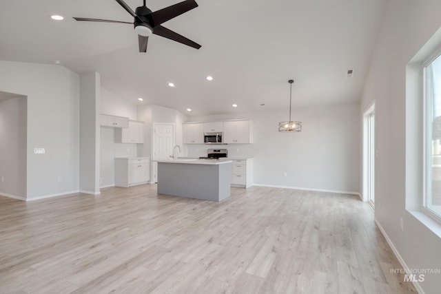 kitchen with a center island with sink, white cabinets, hanging light fixtures, stainless steel appliances, and light countertops