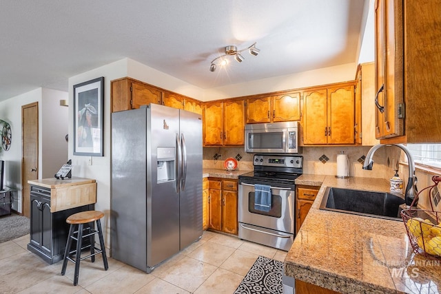 kitchen with appliances with stainless steel finishes, brown cabinetry, a sink, and tasteful backsplash
