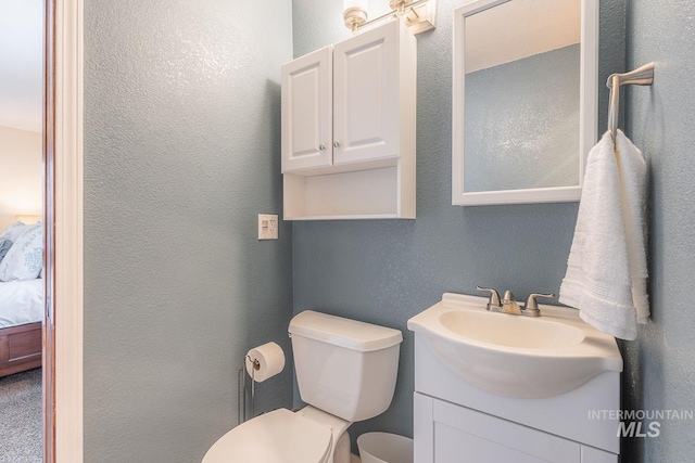 bathroom with connected bathroom, toilet, a textured wall, and vanity