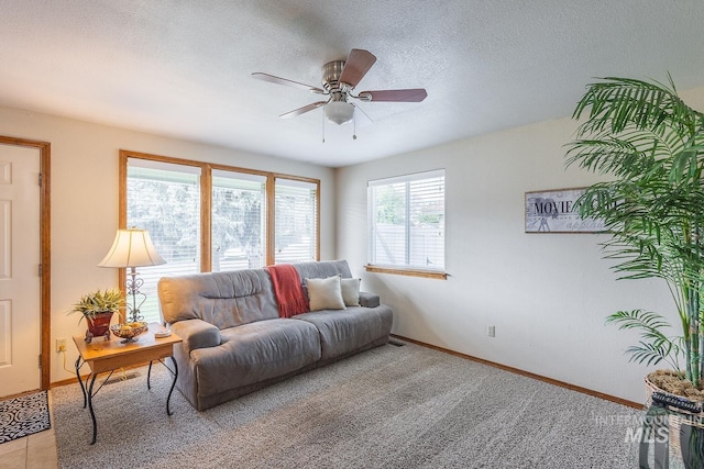 living room with baseboards, a textured ceiling, ceiling fan, and light colored carpet