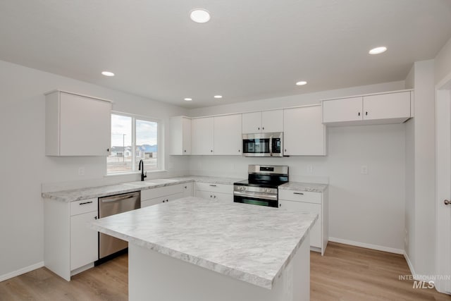 kitchen with sink, appliances with stainless steel finishes, white cabinetry, light hardwood / wood-style floors, and a kitchen island