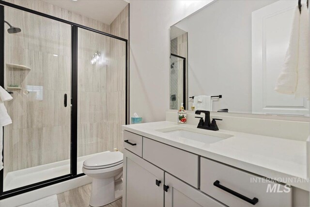 bathroom with hardwood / wood-style flooring, vanity, an enclosed shower, and toilet