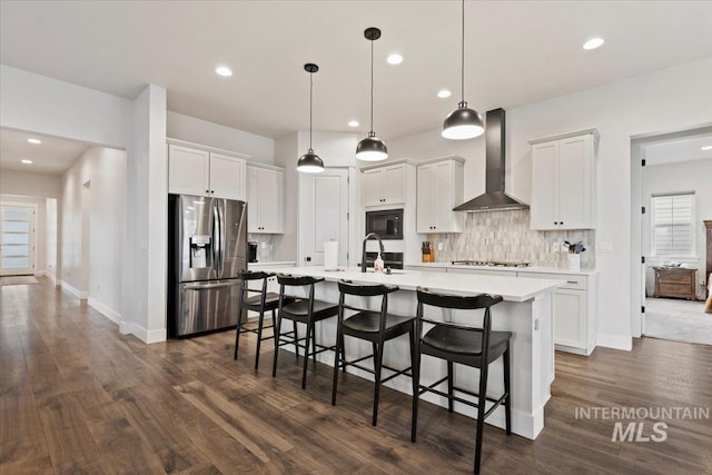 kitchen with decorative light fixtures, stainless steel appliances, white cabinetry, and wall chimney exhaust hood