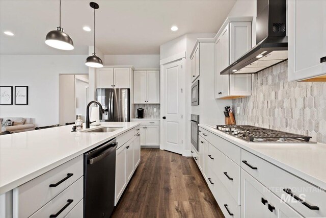 kitchen featuring pendant lighting, wall chimney range hood, sink, white cabinetry, and stainless steel appliances