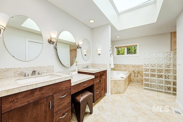 full bath featuring a garden tub, two vanities, a skylight, marble finish floors, and recessed lighting