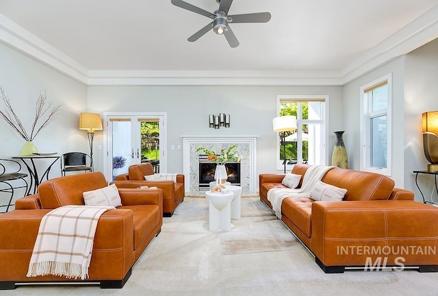 living area with ornamental molding, a ceiling fan, a high end fireplace, and carpet