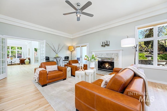 living room featuring light wood finished floors, a premium fireplace, ceiling fan, and baseboards
