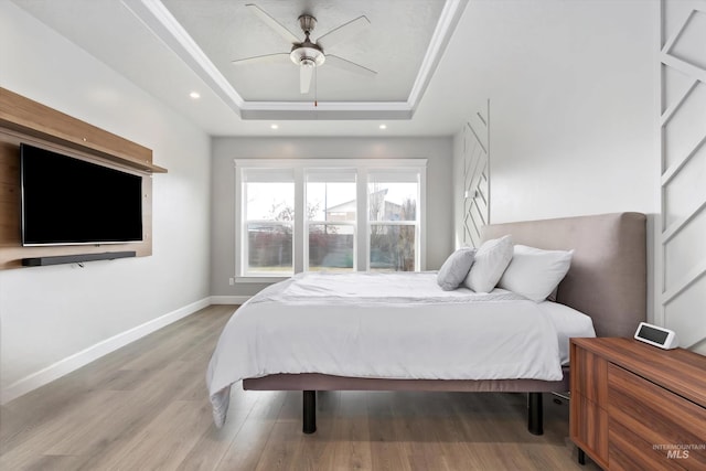 bedroom with baseboards, a ceiling fan, a tray ceiling, light wood-type flooring, and recessed lighting