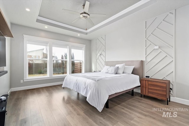 bedroom with a tray ceiling, recessed lighting, ornamental molding, wood finished floors, and baseboards