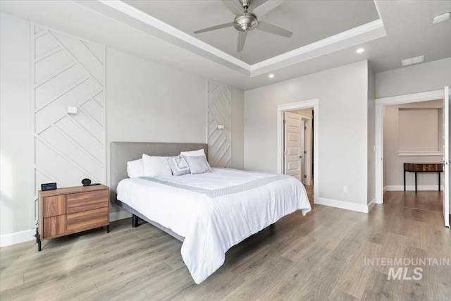 bedroom with light wood finished floors, baseboards, visible vents, and a tray ceiling