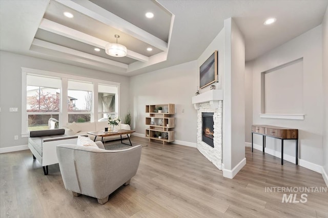 living area featuring light wood-type flooring, baseboards, a raised ceiling, and a stone fireplace