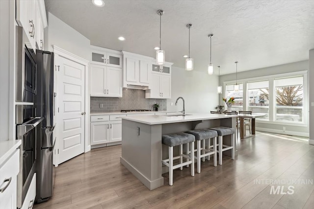 kitchen with light countertops, decorative backsplash, a sink, wood finished floors, and a kitchen bar