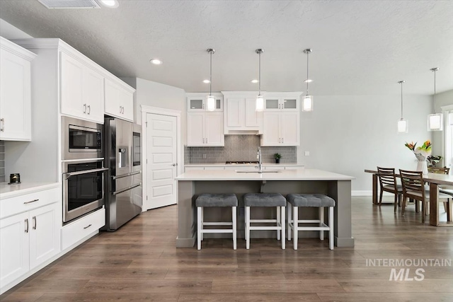 kitchen with built in appliances, white cabinets, light countertops, tasteful backsplash, and glass insert cabinets