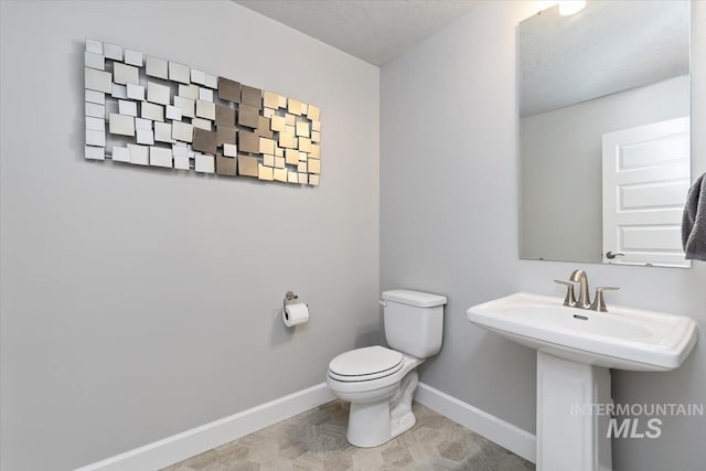 half bath featuring a sink, toilet, and baseboards