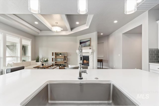 kitchen with a sink, a warm lit fireplace, open floor plan, and light countertops