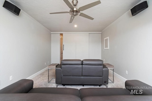 living area featuring carpet, baseboards, ceiling fan, and a textured ceiling