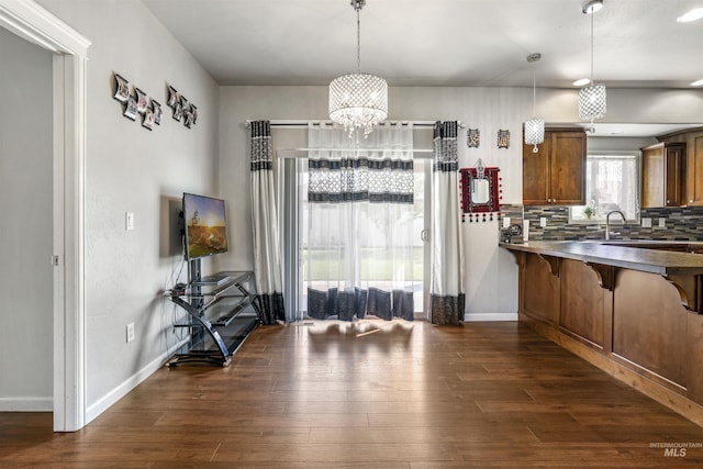 kitchen with a breakfast bar area, a notable chandelier, decorative backsplash, and dark wood-style flooring