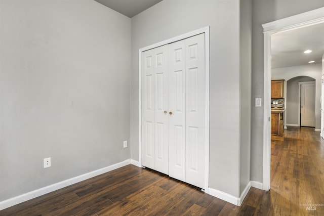 unfurnished bedroom featuring a closet, dark wood-type flooring, baseboards, arched walkways, and recessed lighting