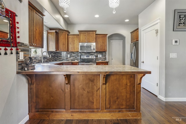 kitchen featuring a sink, a peninsula, stainless steel appliances, arched walkways, and decorative backsplash