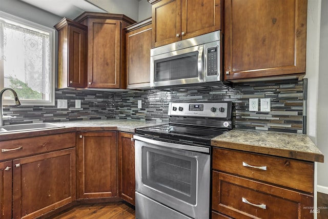 kitchen with light countertops, a sink, backsplash, appliances with stainless steel finishes, and dark wood-style flooring