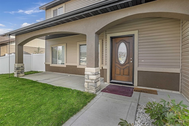 doorway to property featuring a lawn, fence, and stucco siding