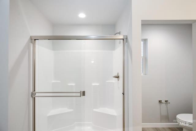 bathroom with wood finished floors, a shower stall, toilet, and baseboards