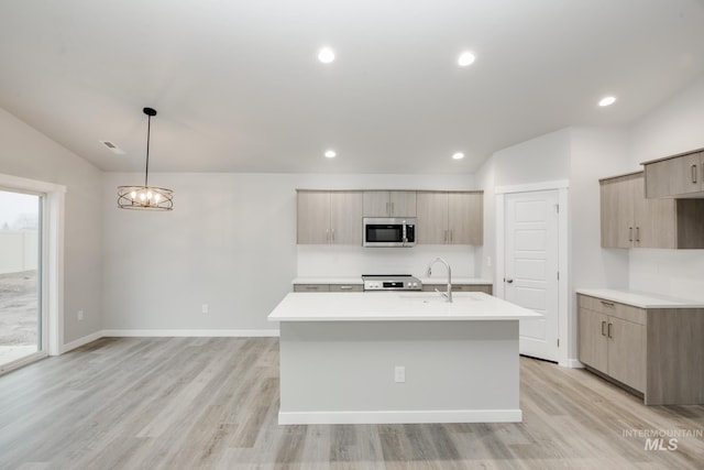 kitchen with a kitchen island with sink, a sink, light countertops, stainless steel microwave, and modern cabinets