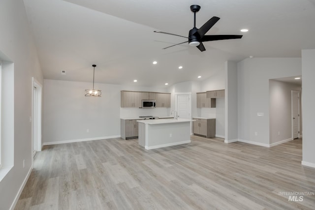 kitchen featuring light wood-style floors, open floor plan, light countertops, stainless steel microwave, and an island with sink