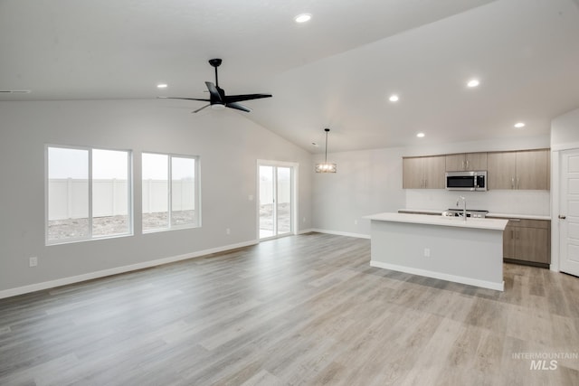 kitchen with light countertops, stainless steel microwave, open floor plan, a kitchen island with sink, and light wood-type flooring