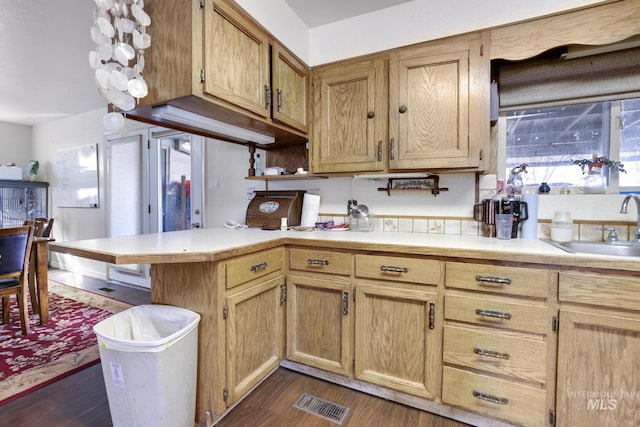 kitchen with visible vents, a sink, a peninsula, light countertops, and dark wood-style flooring