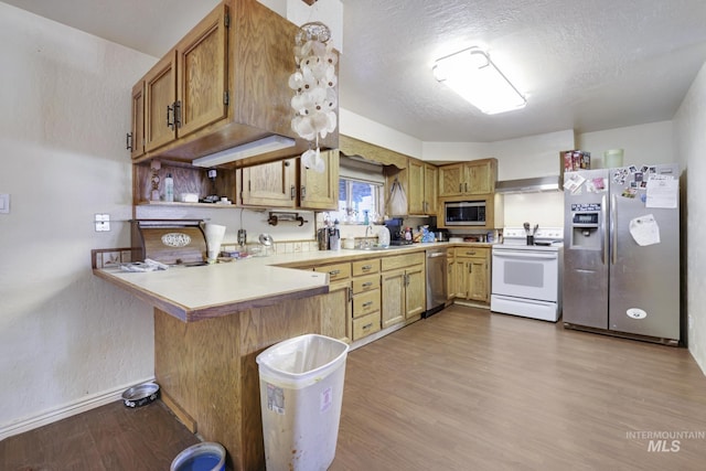 kitchen with wood finished floors, a peninsula, light countertops, appliances with stainless steel finishes, and a textured ceiling