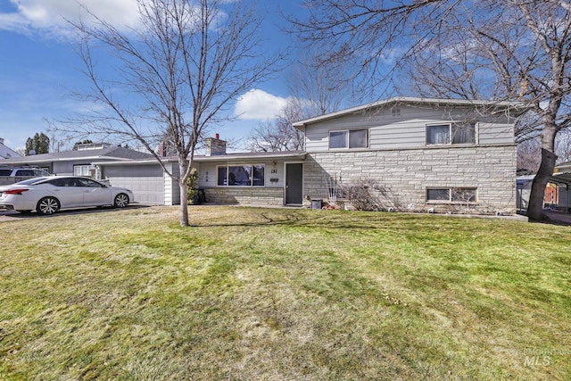 tri-level home with stone siding, an attached garage, a chimney, and a front lawn