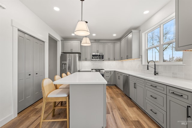 kitchen featuring a breakfast bar, stainless steel appliances, sink, gray cabinets, and a kitchen island