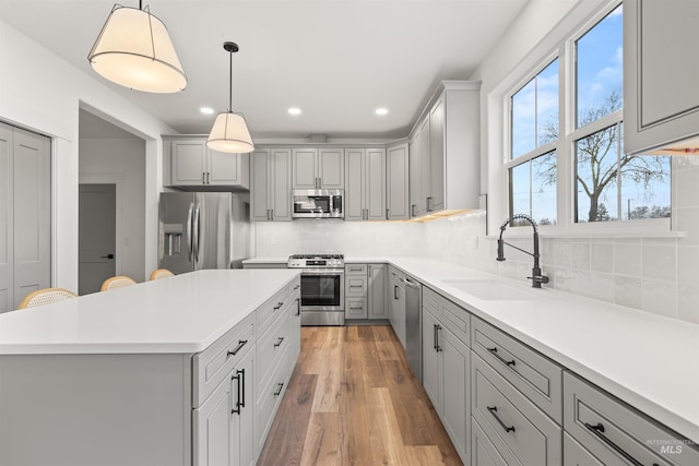 kitchen with hanging light fixtures, gray cabinets, sink, and stainless steel appliances